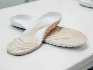 Twee op maat gemaakte orthopedische inlegzolen op wit klinisch oppervlak, één met slijtagepatronen, de ander met 3D-geprinte textuur.