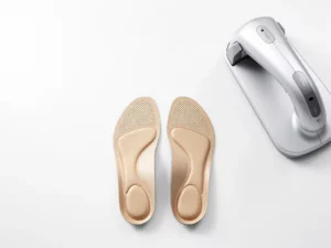 Op maat gemaakte orthopedische inlegzolen naast een 3D-voetscanner op een wit klinisch oppervlak, bovenaanzicht.