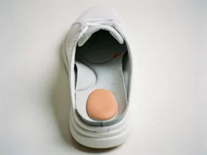 Op maat gemaakte orthopedische inlegzool met gewelfde steunboog in een open witte schoen op wit oppervlak.