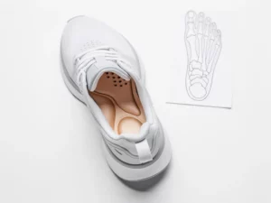 Op maat gemaakte orthopedische inlegzool in een minimalistische hardloopschoen, met voetanatomie referentie op witte ondergrond.