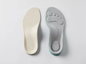 Standaard schuim inlegzool naast een op maat gemaakt orthopedisch steunzool met zichtbare voetboogvorm op witte ondergrond.