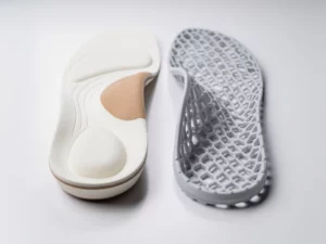Gefreesd orthopedisch inlegzool naast een 3D-geprint lattice inlegzool op witte klinische ondergrond, detailopname.