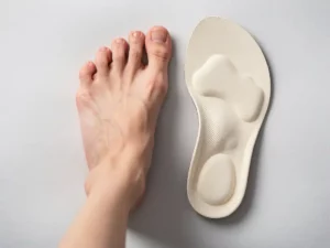 Blote voet naast een op maat gemaakte orthopedische inlegzool op een witte medische ondergrond, bovenaanzicht.