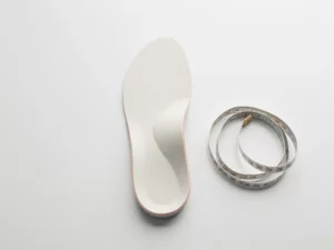 Op maat gemaakte orthopedische inlegzool op wit klinisch oppervlak met meetlint, vlakke bovenaanzicht studiobelichting.