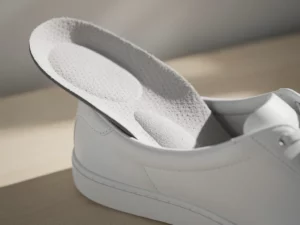 Orthopedische inlegzool in witte sneaker op houten ondergrond, close-up met zachte studiolicht op gestructureerd schuimoppervlak.