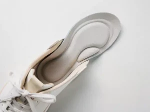 Dunne orthopedische inlegzolen in een minimalistische schoen op wit oppervlak, bovenaanzicht met zachte schaduwen en contourvormen.
