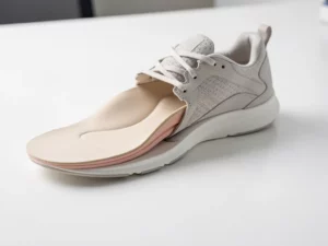 Op maat gemaakte orthopedische inlegzool gedeeltelijk uit atletische schoen getrokken, met zichtbare gewelfde voetboogondersteuning op wit klinisch oppervlak.
