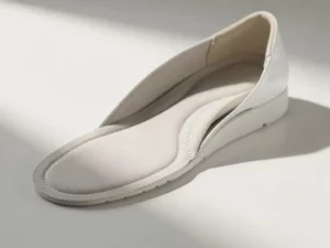 Aangepaste orthopedische inlegzool in een witte minimalistische schoen op een klinisch witte ondergrond, zachte natuurlijke belichting.