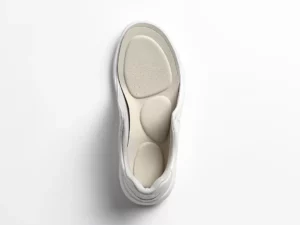 Orthopedische inlegzolen in witte sneaker, zacht schuimoppervlak zichtbaar, bovenaanzicht op witte achtergrond.